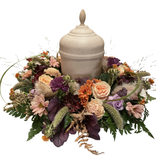 En dekorativ urna omgiven av en krans av färgglada blommor, inklusive rosor, prästkragar och olika lövverk.