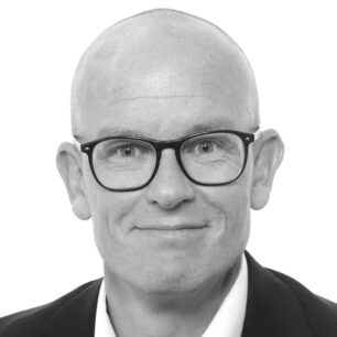 En man med glasögon och rakad skalle ler mot kameran.