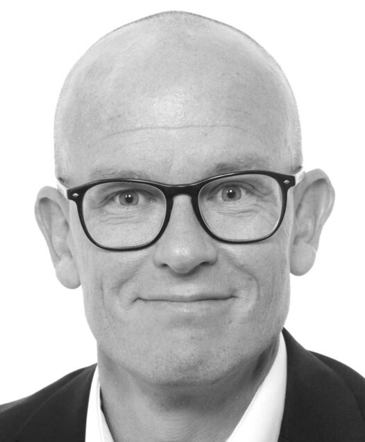 En man med glasögon och rakad skalle ler mot kameran.
