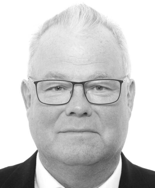 En man med kort ljust hår och glasögon ler mot kameran.