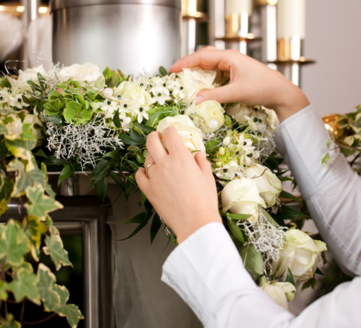 Händer som arrangerar vita blommor och grönt lövverk på en dekor.