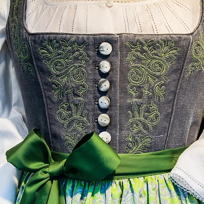 Närbild av en traditionell folkdräkt med broderad livstycke och grön rosett.
